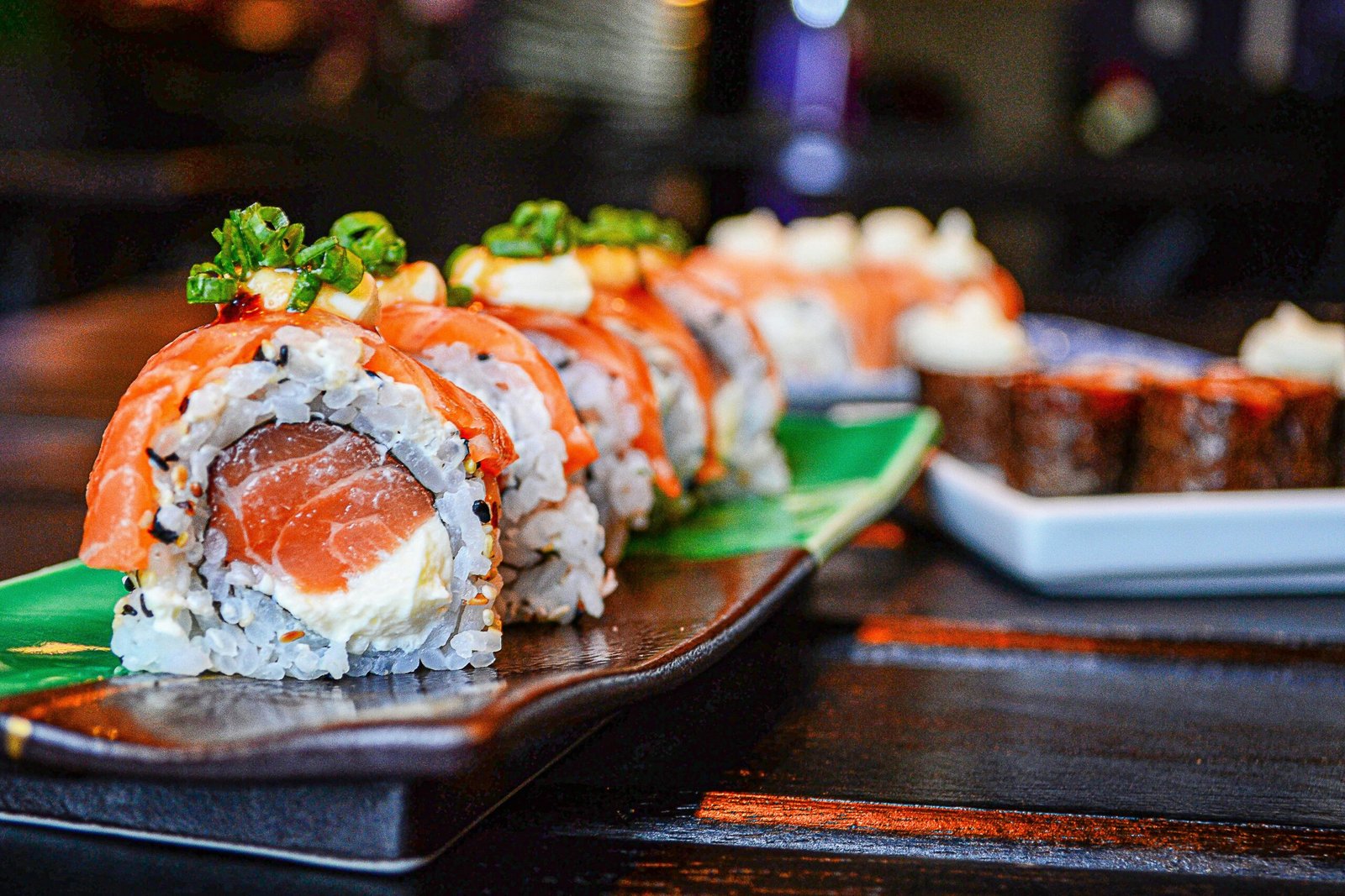 Delicious sushi rolls with salmon and cream cheese garnished with green onions, presented on a ceramic plate.